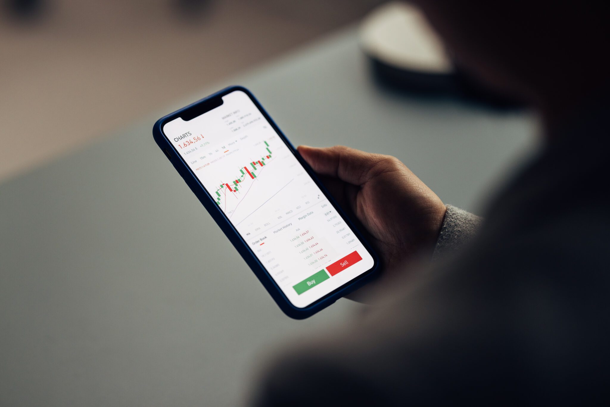 Over-the-shoulder view of a person analyzing stock market charts on a smartphone, concept of mobile trading.